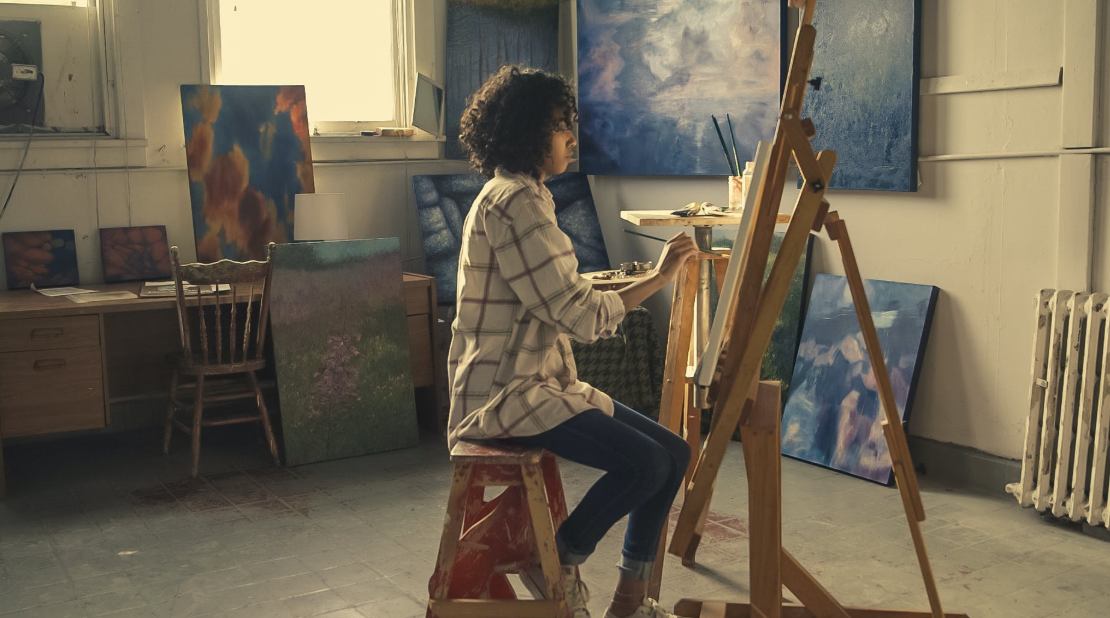 woman sitting in front of an easel painting
